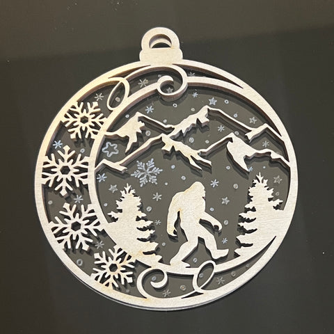 Two part ornament, Bigfoot-Sasquatch-Yeti walking through a mountain scene with snowflakes falling all around. This photo was shot on a black background, the acrylic is actually clear like in the next photo. - Dailey Woodworking