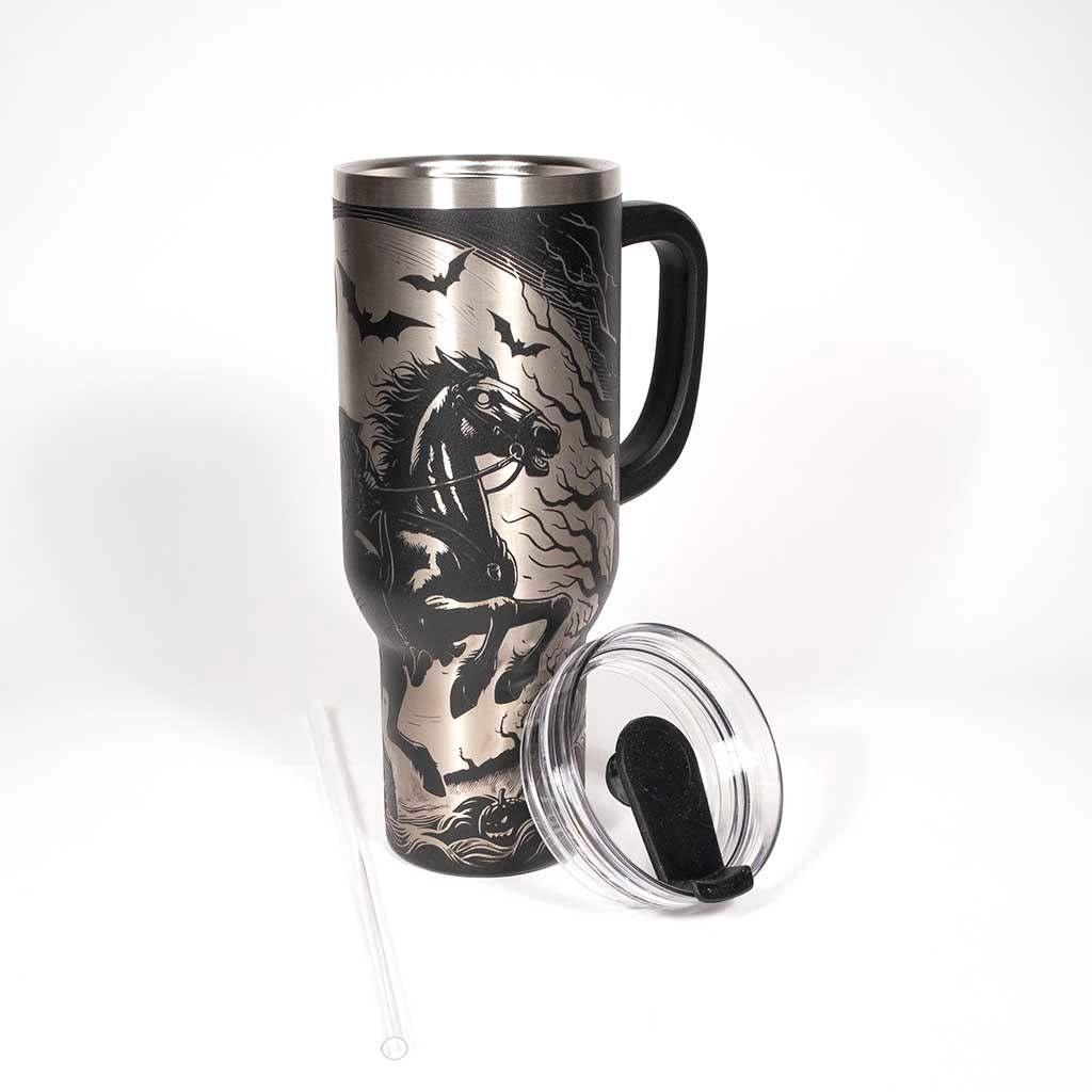 This is a black 40 ounce tumbler with a screw on lid with a drinking hole access and a straw. The laser engraving is of a headless horseman on his trusty steed. With the cover off and straw laying beside the tumbler. 