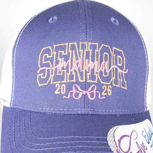 Violet and white cap with 'SENIOR Mama 2026' text on a mannequin head against a white background, close up of lettering