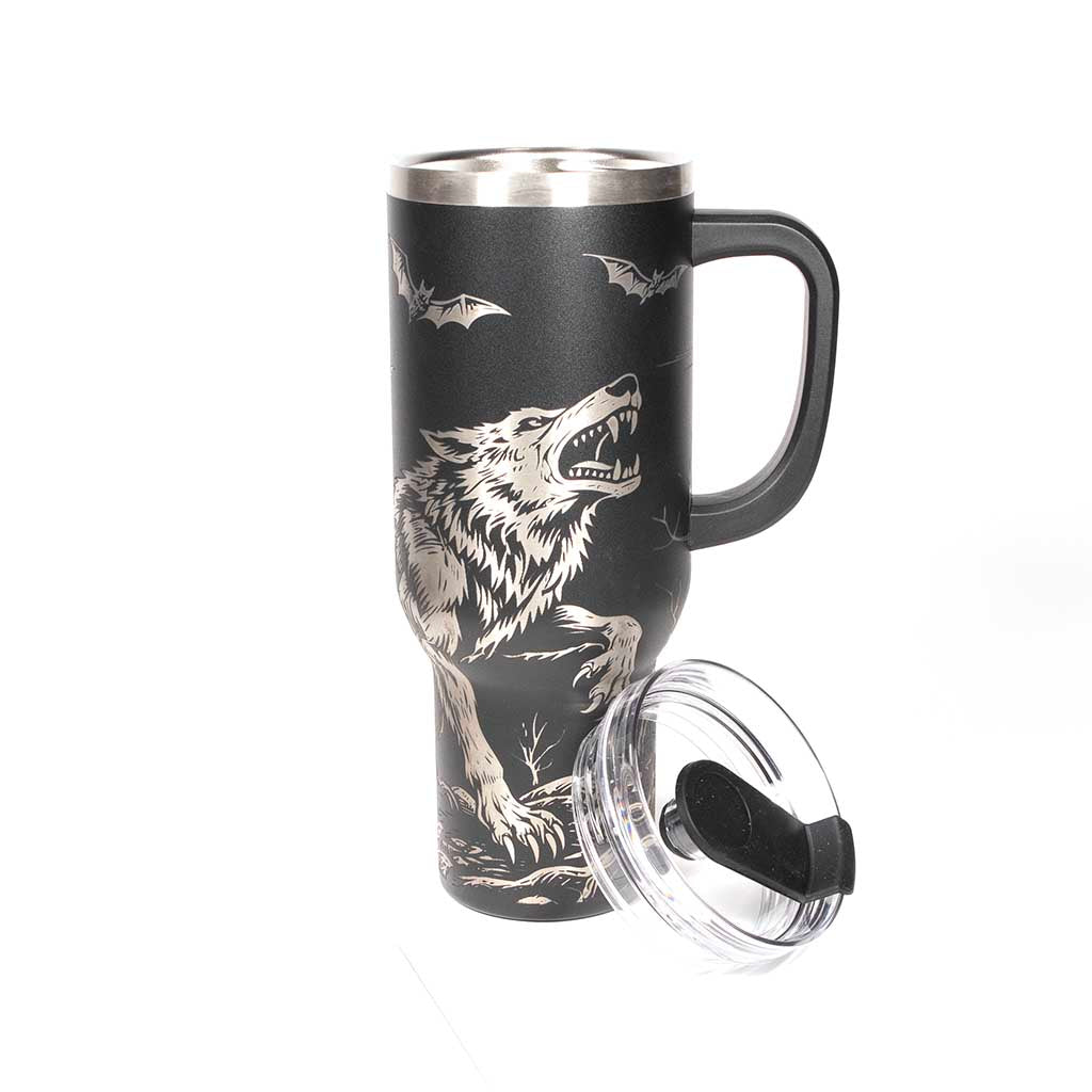 40 ounce travel mug with a werewolf, bats and a gothic cathedral design on a black background. With cover off and straw beside the tumbler. 