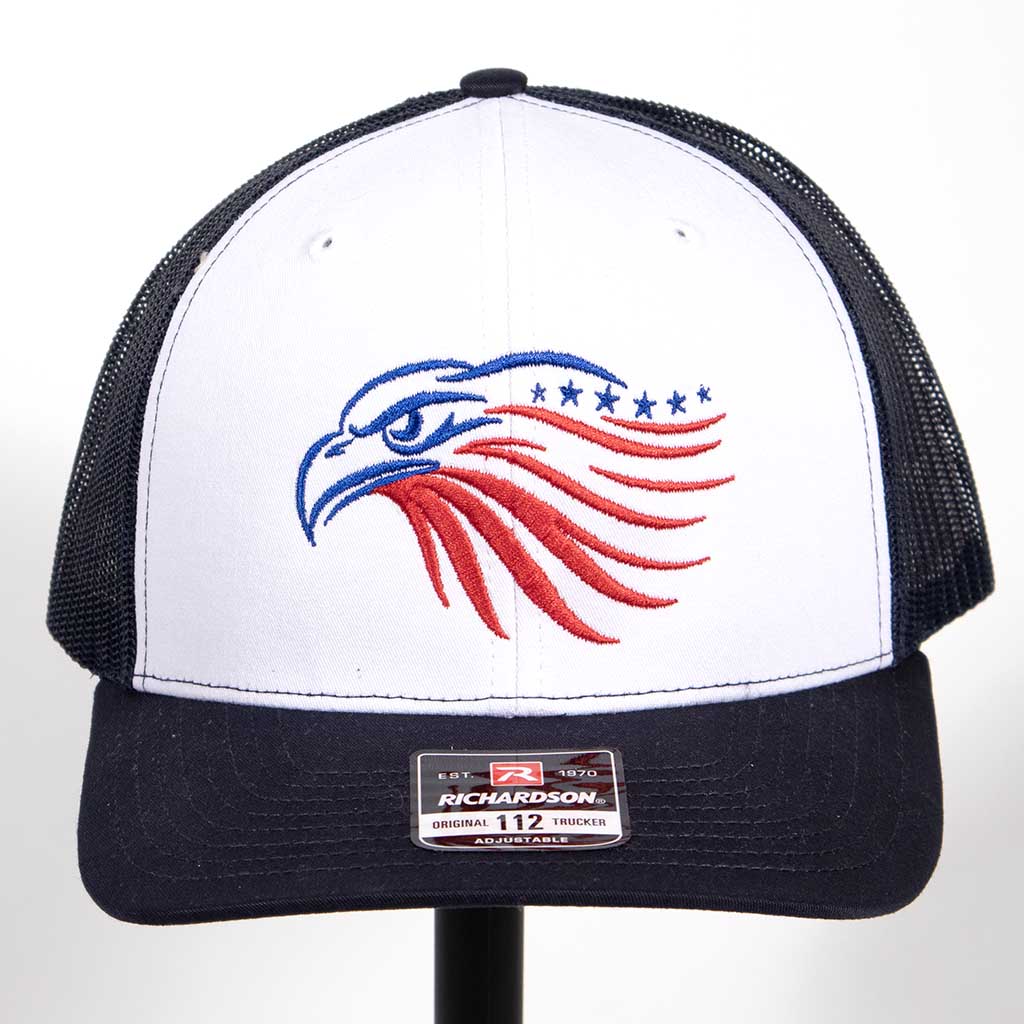This is a Richardson 112 snap back hat with a white front, navy blue bill and navy blue mesh back. The hat has the outline of an eagles head. The head has been embroidered in blue and red stitching. From the front. 