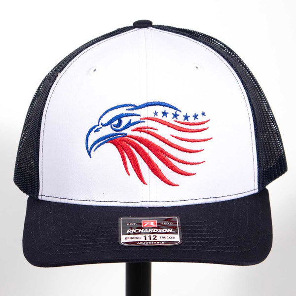 This is a Richardson 112 snap back hat with a white front, navy blue bill and navy blue mesh back. The hat has the outline of an eagles head. The head has been embroidered in blue and red stitching. From the front. 