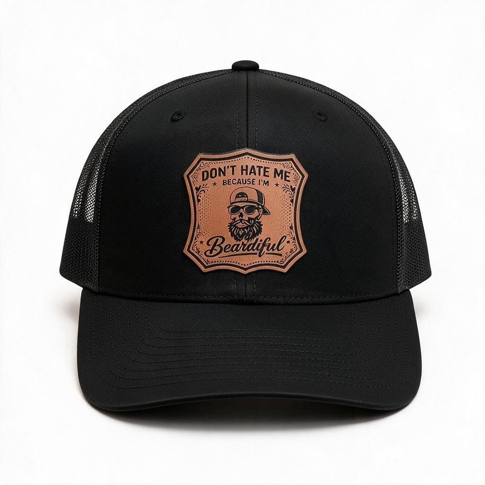 A black trucker-style cap with a brown shield-shaped engraved patch on the front that reads 'DON'T HATE ME BECAUSE I'M Beardiful' with a bearded man wearing a cap.