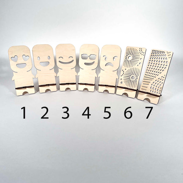 Seven phone stands made from 5mm (approximately 1/4") Birch plywood and the unique designs are laser cut. The designs are #1 Heart Eyes #2 Astonished #3 Smiling #4 Cool Dude #5 Grumpy #6 Starburst #7 Wave - Dailey Woodworking
