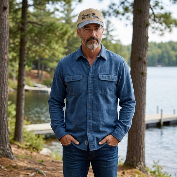 Dailey Woodworking Canton Maine loon embroidered hat worn by a man in a blue flannel shirt by a lake