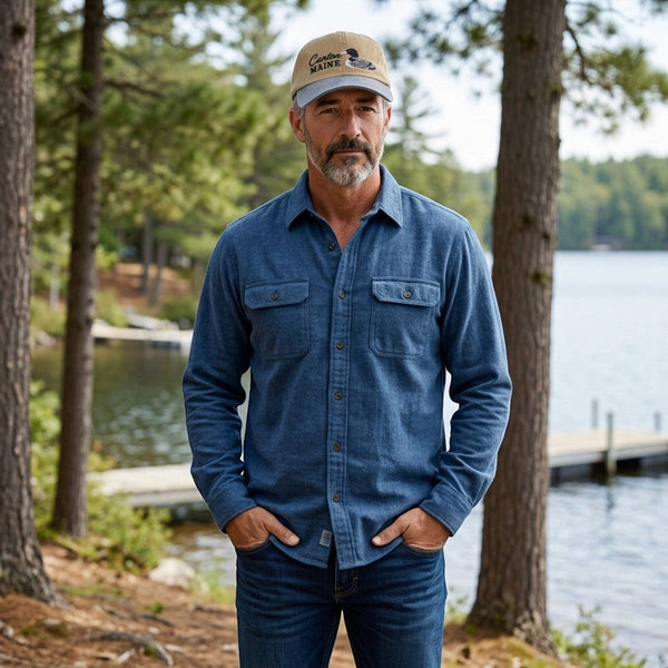 Man wearing a Dailey Woodworking Canton, Maine loon embroidered hat and blue shirt by a lake.