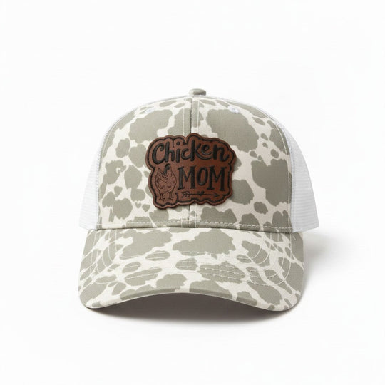 Dailey Woodworking grey cow print trucker hat with "Chicken Mom" leatherette patch and white mesh back.
