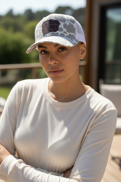 Dailey Woodworking grey cow print trucker hat with white mesh back and a leatherette patch that says "Chicken Mom".