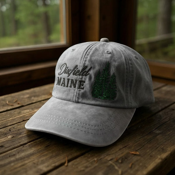 Dailey Woodworking grey garment-washed cotton hat with Dixfield Maine embroidery and pine tree design on wood table