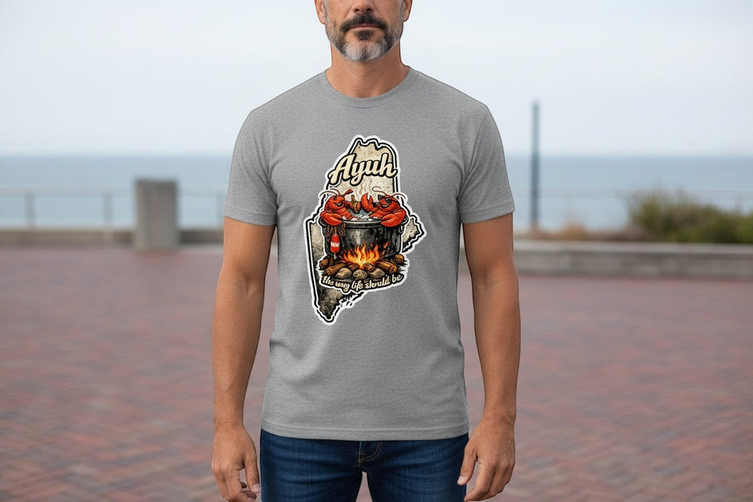 Gravel colored t-shirt with a graphic of the state of Maine containing a lobster pot over a fire with lobsters sitting inside and the words "Ayuh" and "The way life should be"