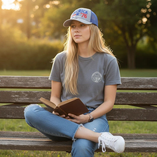 Dailey Woodworking patriotic trucker hat with America 250 embroidery worn by a woman reading on a park bench.