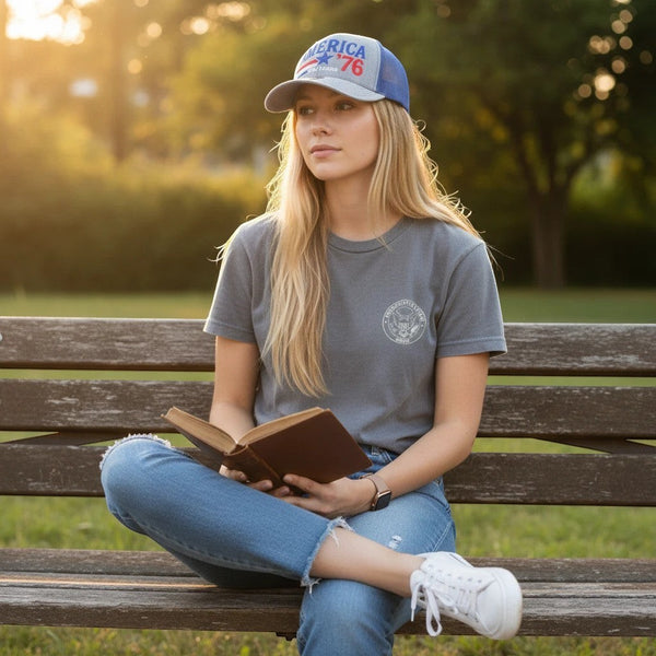 Dailey Woodworking patriotic trucker hat with America 250 embroidery worn by a woman reading on a park bench.