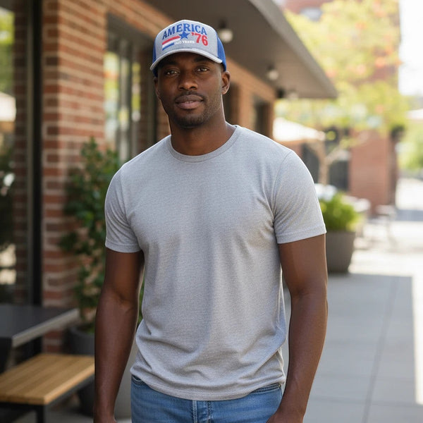 A man wearing a Dailey Woodworking gray and blue patriotic America 250 trucker hat with red 76 embroidery outdoors.