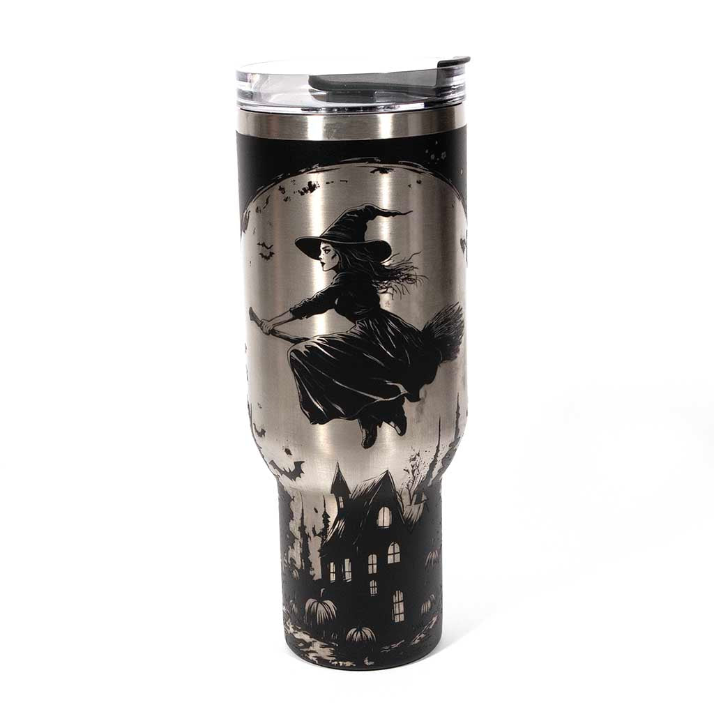 This is a black 40 ounce tumbler with a screw on lid with a drinking hole access and a straw. The laser engraving is of a witch flying on her broom above a home and pumpkin patch. Side 1