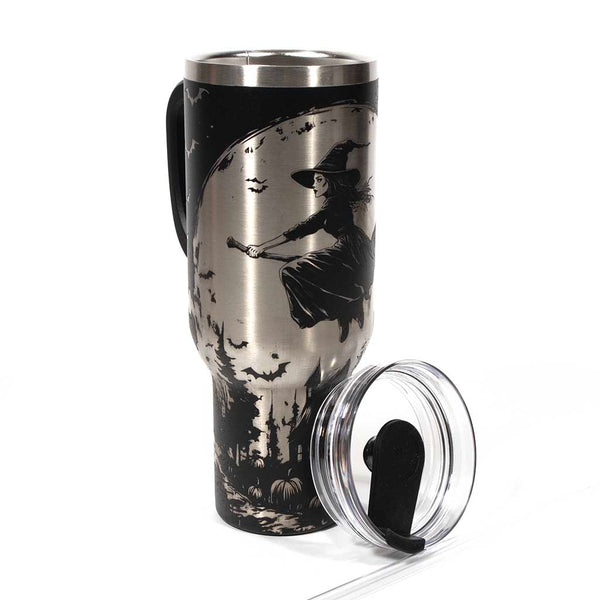 This is a black 40 ounce tumbler with a screw on lid with a drinking hole access and a straw. The laser engraving is of a witch flying on her broom above a home and pumpkin patch. Shown with lid off and straw.