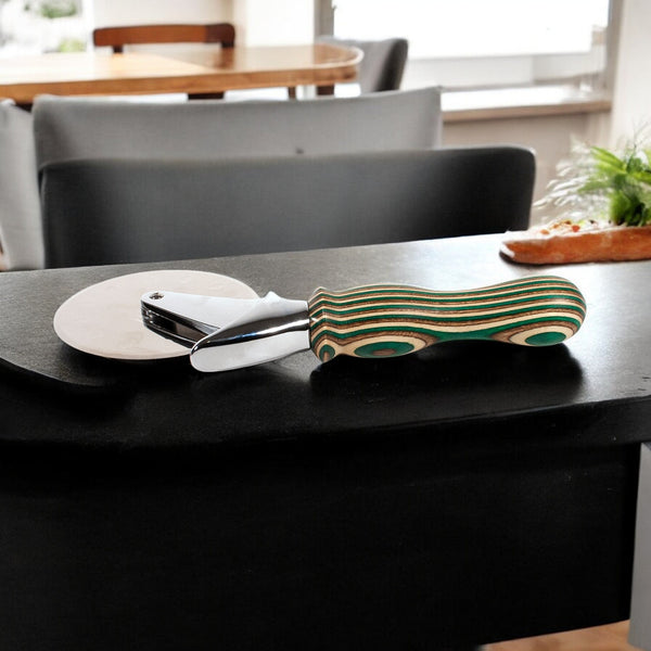 Camo Laminated Pizza Cutter, Pizza Wheel sitting on a black counter with table and chairs in background - Dailey Woodworking